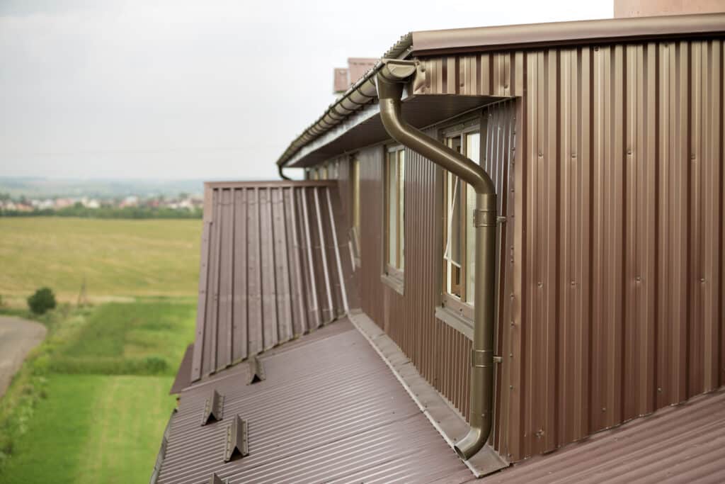 Cottage attic room, roof and walls covered with brown metal siding planks, new gutter system